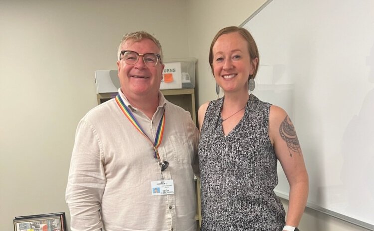 Andrew Lowden (left) and Allison Leece stand together at the DNSWM office. The two, who are Caucasian, are wearing business casual attire. The background includes a whiteboard, office supplies and colorful artwork.