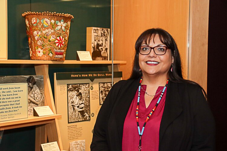 Katrina Furman, the newly appointed Anishinaabe curator and member of the Grand Traverse Band of Ottawa and Chippewa poses in front of examples of basket weaving examples.