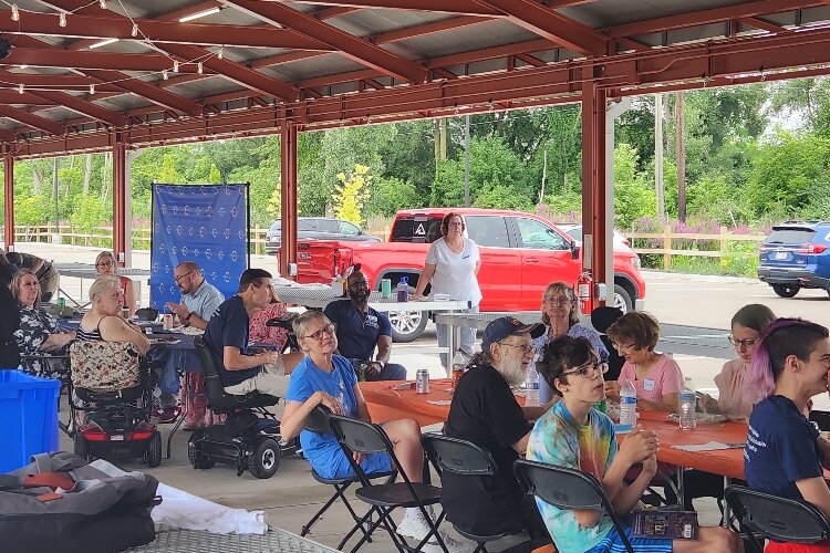 Picture shows people gathered around tables at the Kalamazoo Farmers Market for at DNSWM ADA celebration. 