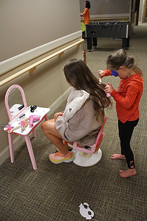 A girl pretends to be a hairdresser with a staff member.